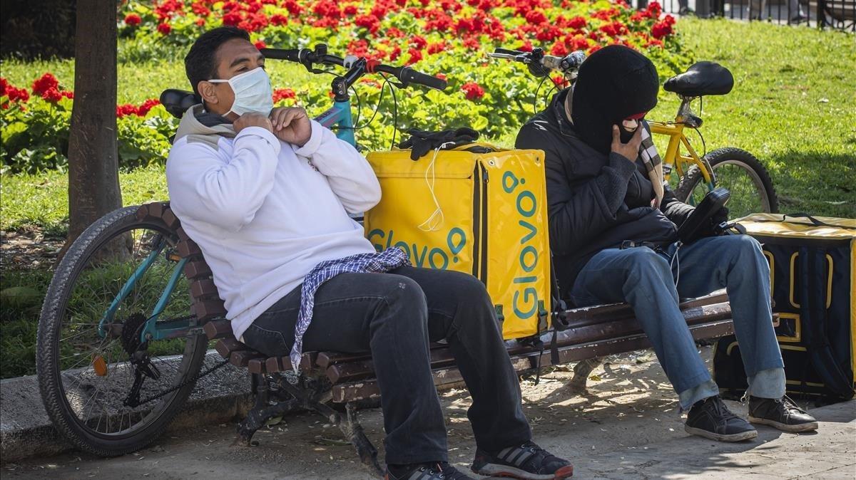 Dos repartidores de comida a domicilio protegidos con mascarillas, en un momento de descanso en Valencia.