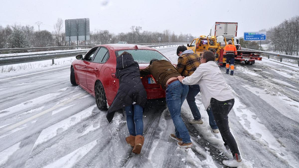 Varias personas empujan un vehículo afectado por la nevada en la  Autovía de la Ruta de la Plata (A-66).