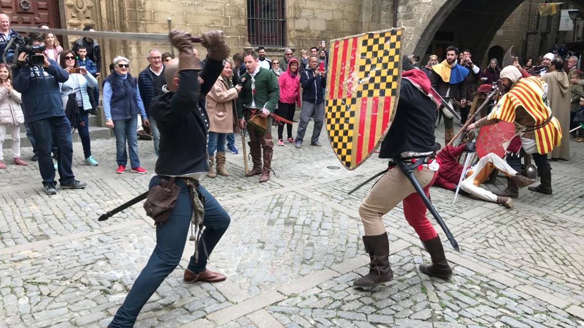 Varios hombres combaten en la plaza de la villa, emulando las peleas de espadachines de la época medieval.