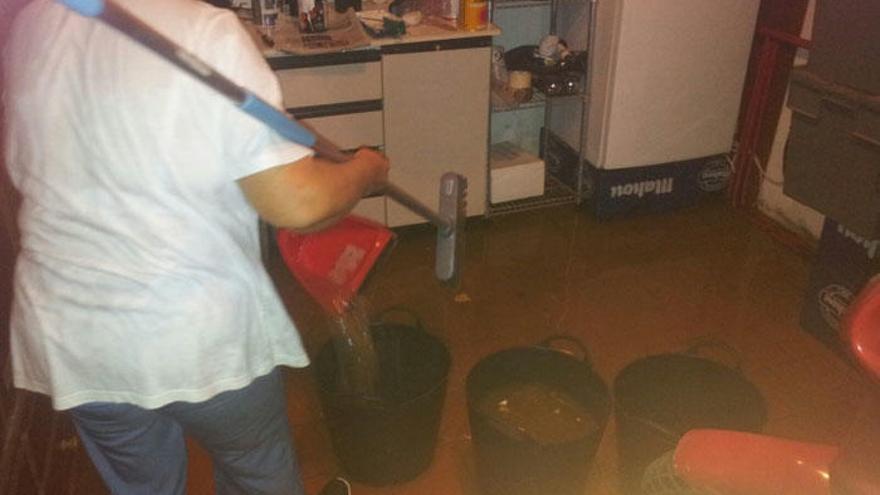 Una vecina de la calle Sierra de Gata recoge el agua de su cocina, inundada tras una tromba.