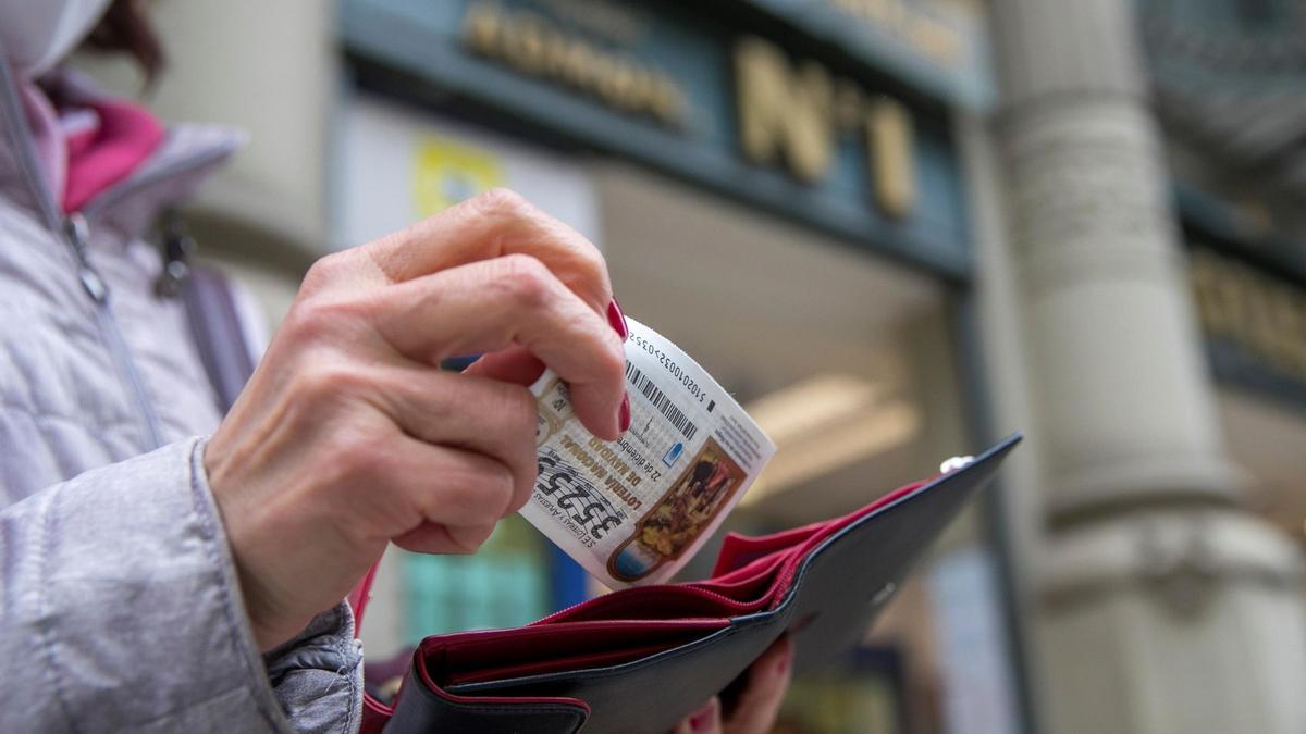 Una clienta de una administración de lotería guardando el décimo en la cartera