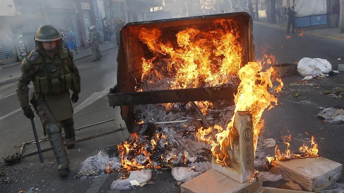 Un policía pasa junto a un contenedor ardiendo en Viña del Mar.