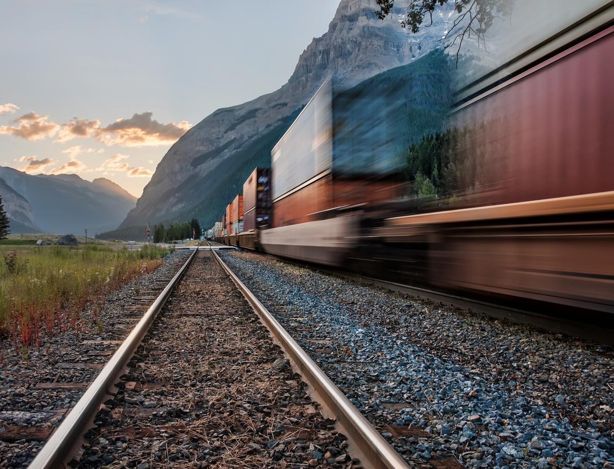 Una vía llena de balasto y un tren de mercancías pasando por el sentido opuesto