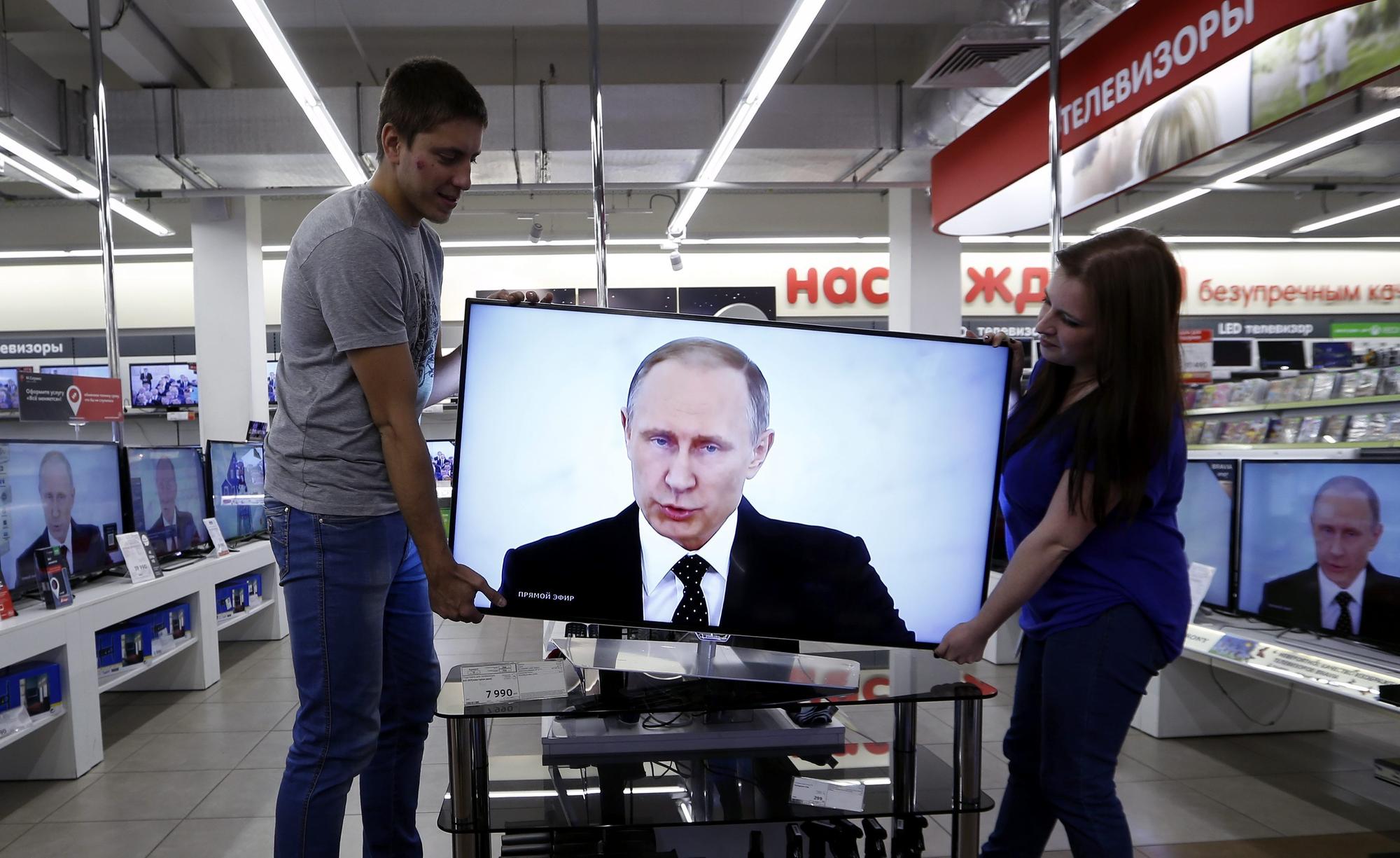 Unos operarios mueven una televisión en la que sale Putin