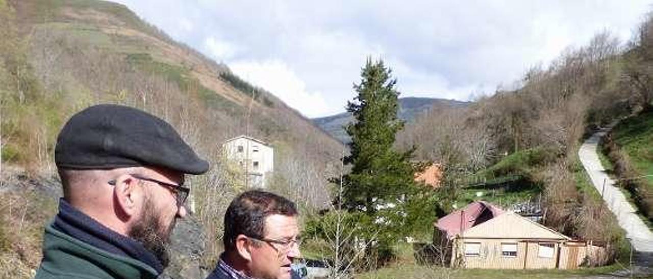 Nicolás López y Segundo Menéndez, ayer, ante una balsa de agua residual procedente de la mina situada en el Coto; al fondo, antiguos edificios de la mina.