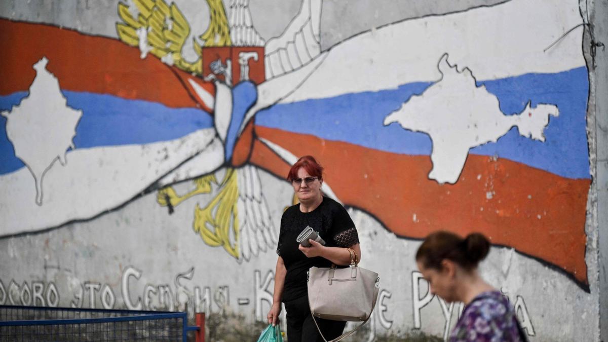 Dos mujeres caminan junto a un mural en el que se lee &quot;Kosobo es Serbia y Crimea es Rusia&quot;, en el norte de la población de Mitrovica, de mayoría serbia.