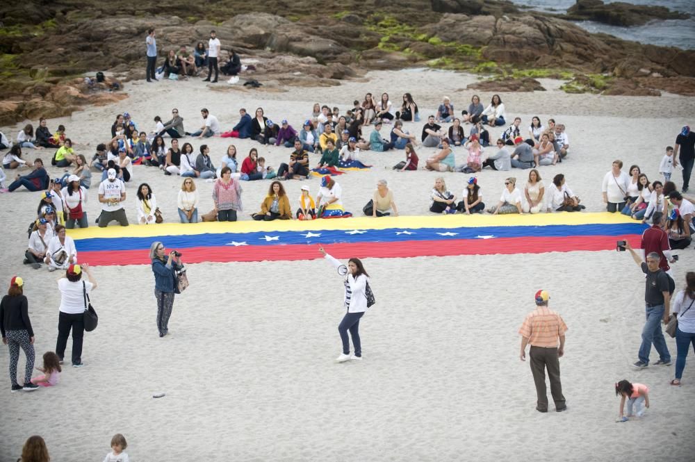 La comunidad venezolana despliega en la playa de Riazor una bandera para exigir que su país sea "libre".