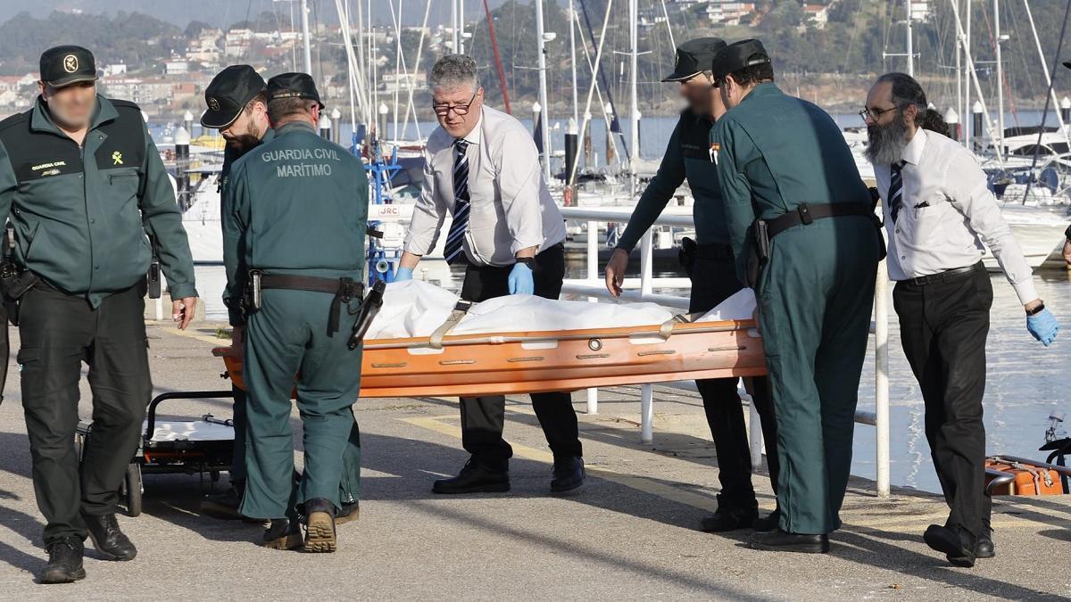 Empleados de la funeraria y efectivos de la Guardia Civil trasladan el cadáver en el puerto de Baiona.