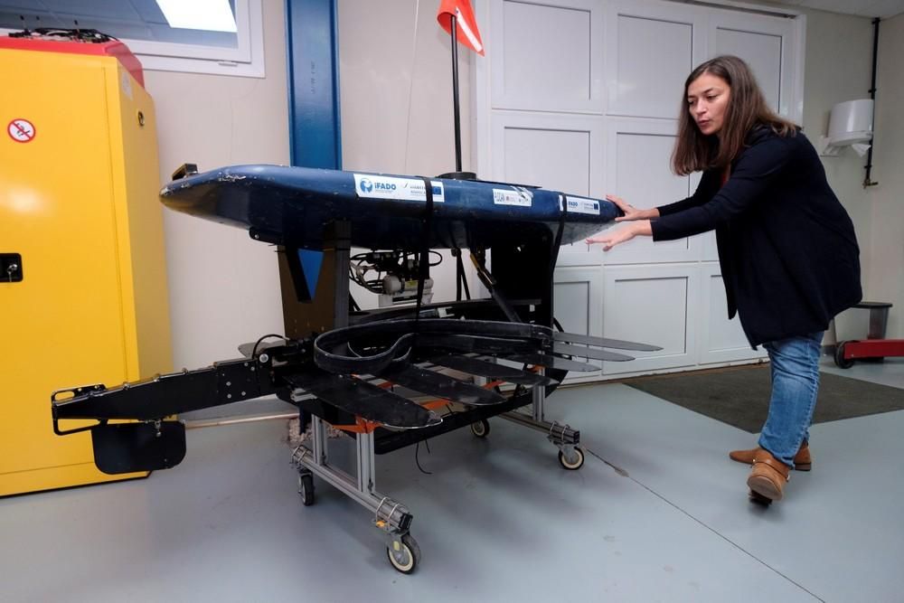 La ingeniera de Robótica de la Plataforma Oceánica de Canarias (Plocán), Tania Morales, muestra el "wave glider" (un robot que navega por la superficie impulsado por la energía de las olas) que ha recorrido en los dos últimos meses 2.000 kilómetros entre los archipiélagos de Azores, Madeira y Canarias recopilando datos sobre el océano, los cetáceos y el ruido del tráfico marítimo. Detrás de ella, un planeador submarino (en amarillo) y un navegador de superficie a vela (azul).