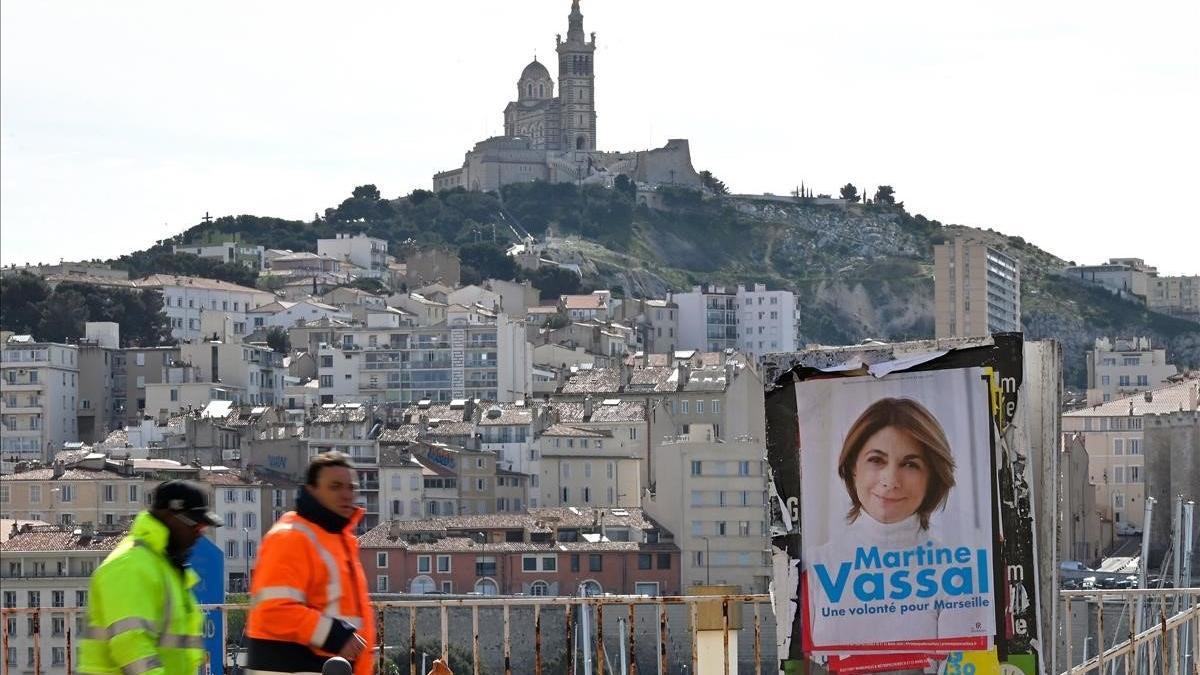 Unos trabajadores pasan junto a un cartel electoral de Martine Vassal, la candidata de Los Republicanos para las elecciones a la alcaldía de Marsella.