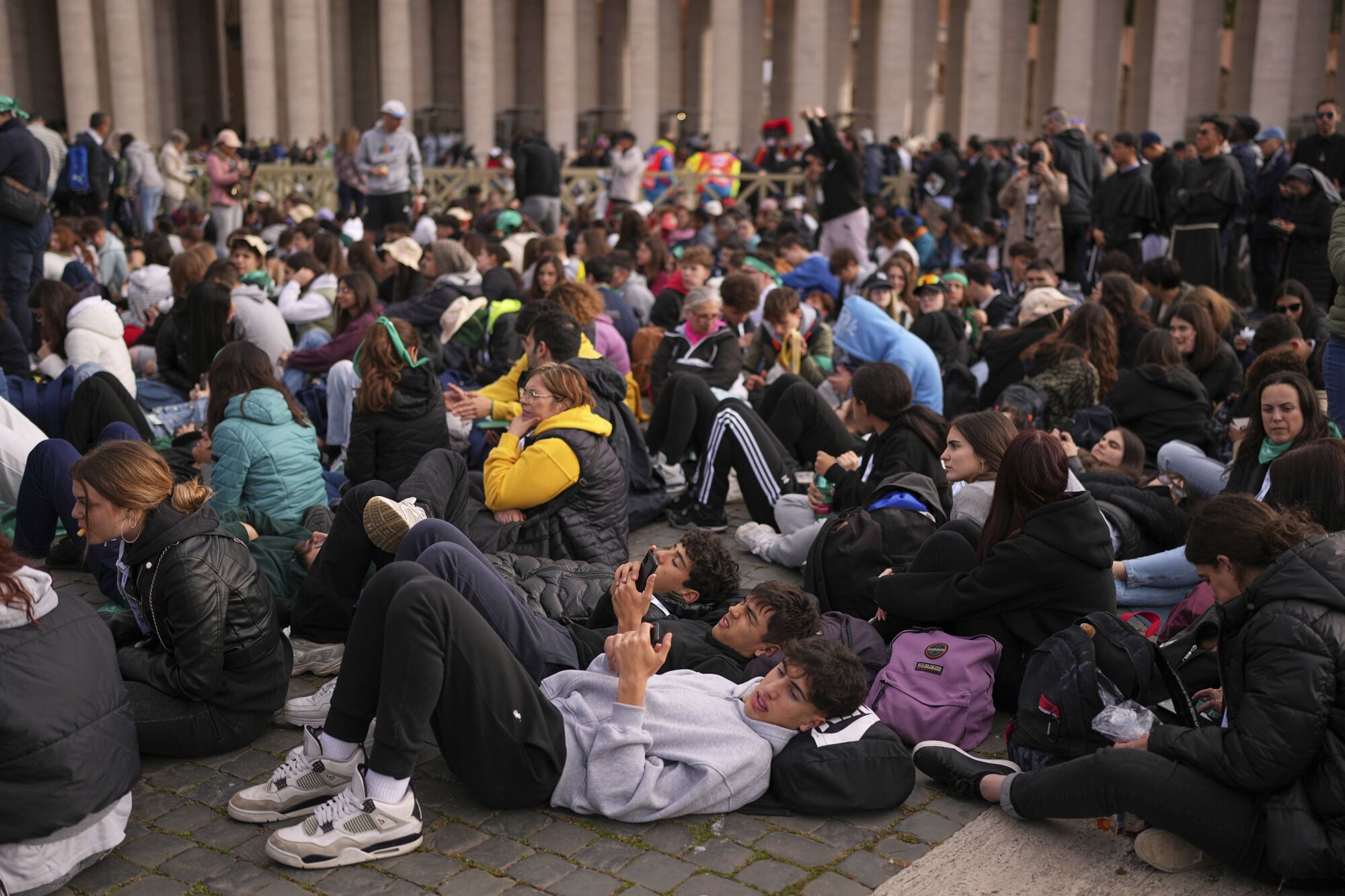 People lie on the pavement while waiting for the funeral of Pope Francis in St. Peter's Square at the Vatican, Saturday, April 26, 2025. (AP Photo/Andreea Alexandru). EDITORIAL USE ONLY/ONLY ITALY AND SPAIN