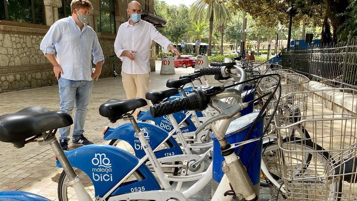 Los concejales de Adelante Nicolás Sguiglia (i) y Eduardo Zorrilla (d) junto a una estación de Málaga Bici, alquiler de bicicletas.