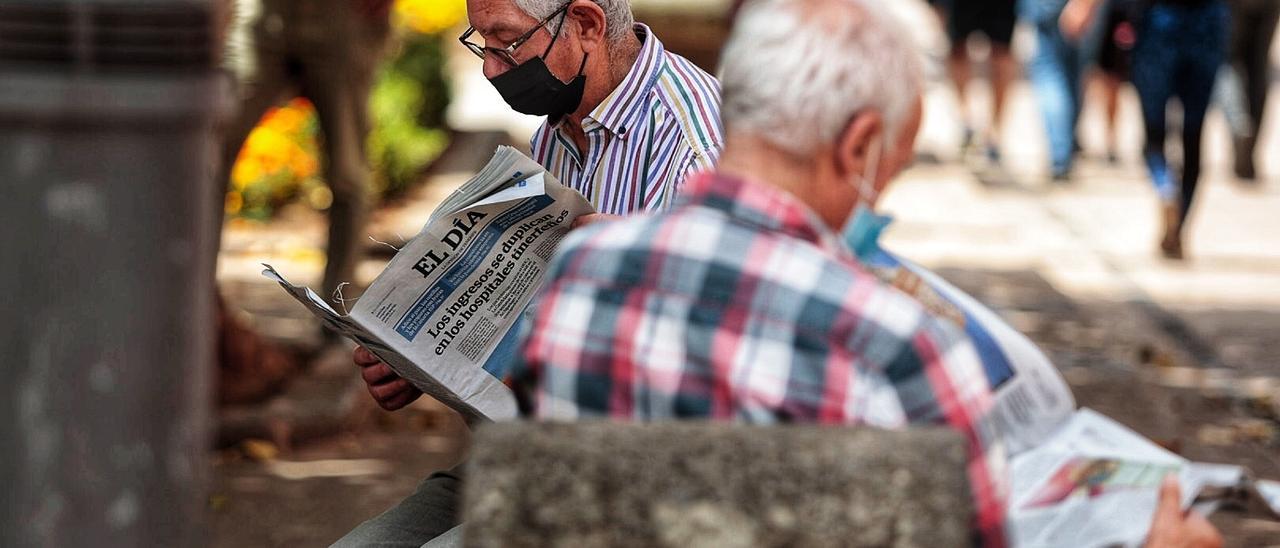 Dos hombres leen un ejemplar pasado del periódico &#039;El Día&#039; sentados en un banco.