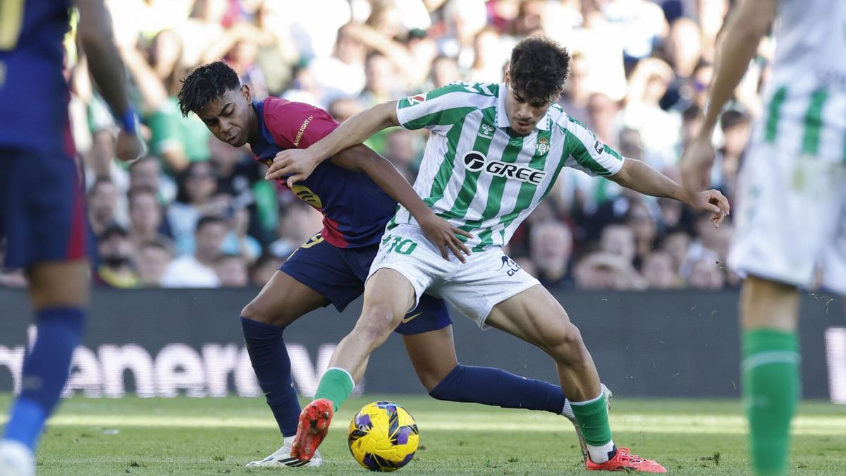 El delantero español del FC Barcelona Lamine Yamal (i) disputa un balón con el delantero hispano-marroquí del Betis Ez Abde (d) durante el partido de la jornada décimo sexta de LaLiga EA Sports que disputan este sábado Real Betis Balompié y FC Barcelona en el Estadio Benito Villamarín de Sevilla. EFE/ Julio Muñoz