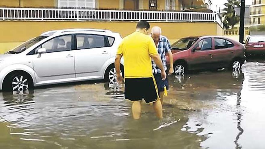 Dos vecinos intentan destapar una alcantarilla para evacuar el agua acumulada.