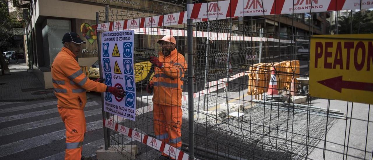 Trabajadores de la empresa a la que se ha adjudicado la reforma de la calle colocan un cartel con indicaciones sobre las condiciones de seguridad