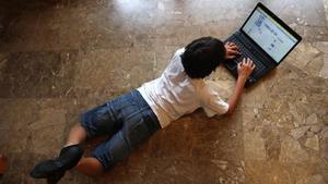 Un niño navega por internet tumbado en el suelo de su casa. 