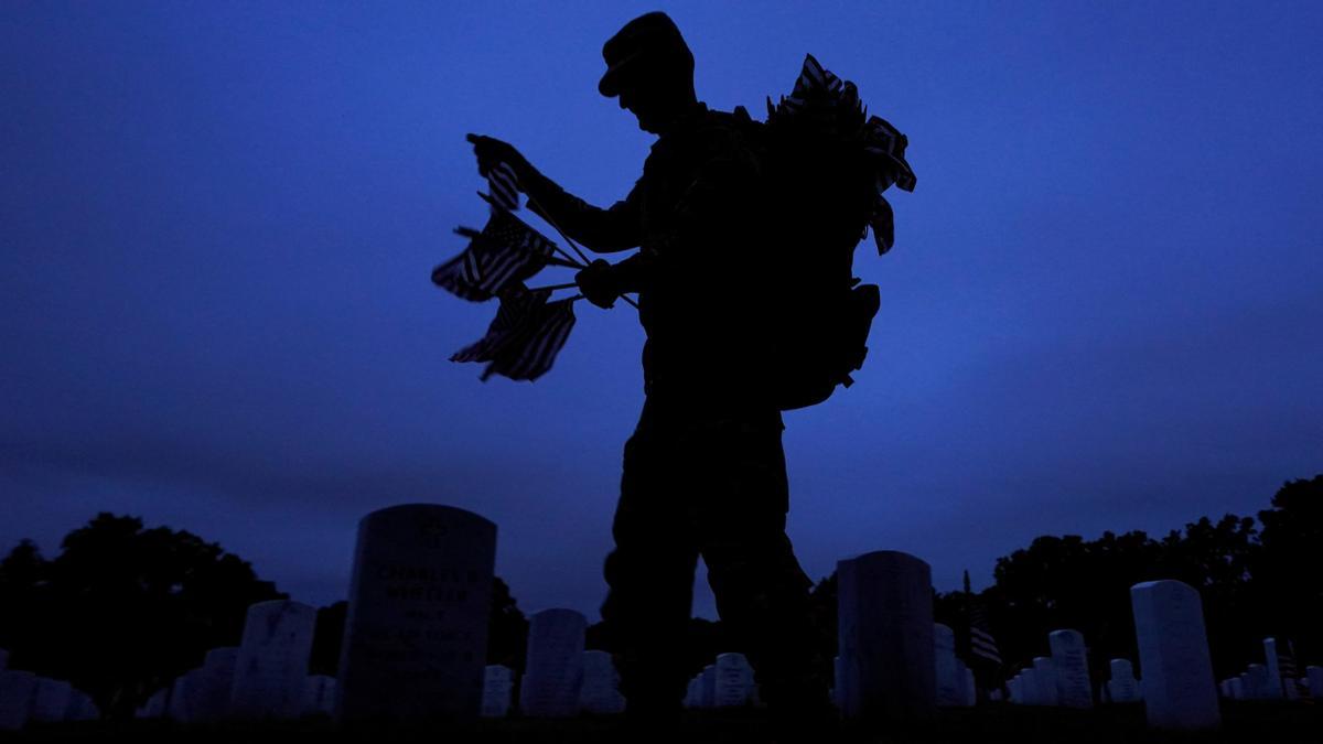 Antes del amanecer, un soldado del Tercer Regimiento de Infantería de EE. UU. coloca banderas en lápidas antes del Día de los Caídos,