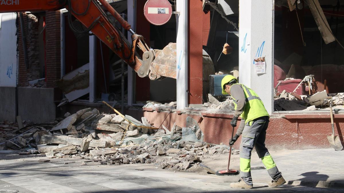 Un operari escombra el carrer mentre la maquina enderroca l'interior de la planta baixa de l'Obrera de Sabadell