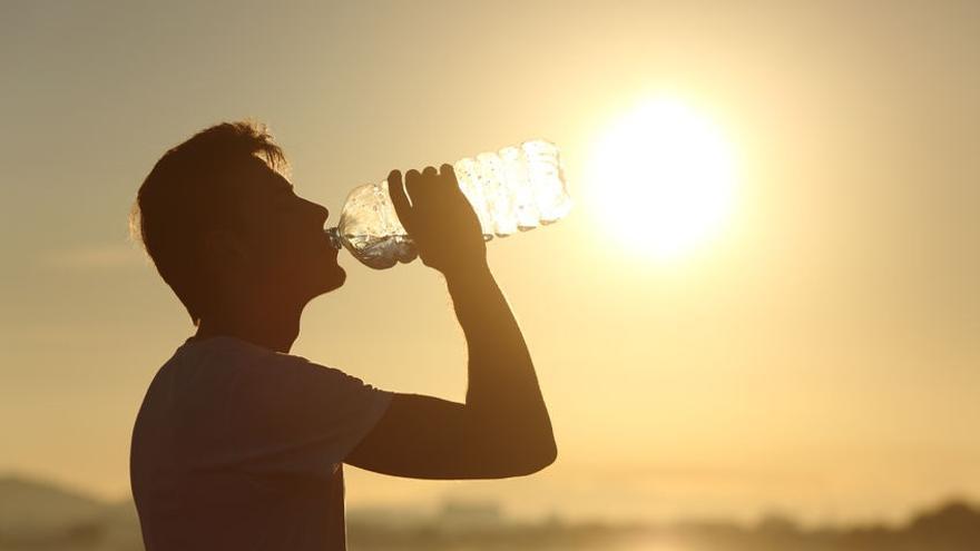 Hitzewelle - ein Mann trinkt am Strand aus einer Wasserflasche.