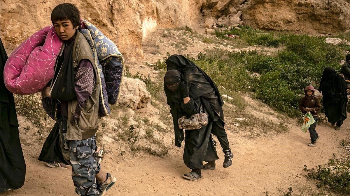 Una mujer que lleva un velo de niqab lleva otra en la espalda mientras caminan con otras personas que se dice que son miembros del grupo IS del Estado Islámico por las Fuerzas Democráticas Sirias