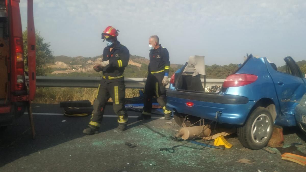 Dos bomberos junto a uno de los vehículos implicados en el accidente de la N-432 entre Córdoba y Espiel.