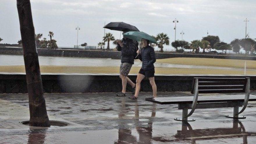 Dos personas pasean bajo la lluvia en la avenida marítima junto a El Reducto, en Arrecife.