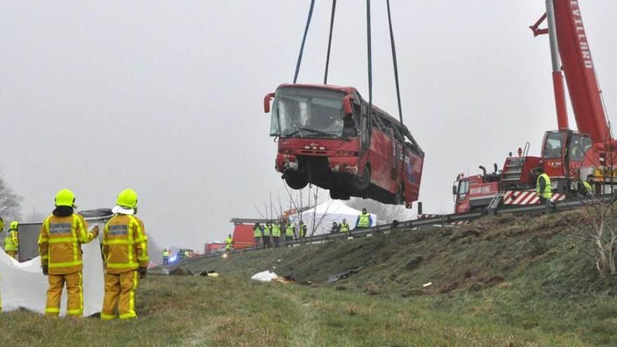 Una grúa eleva el autocar siniestrado.