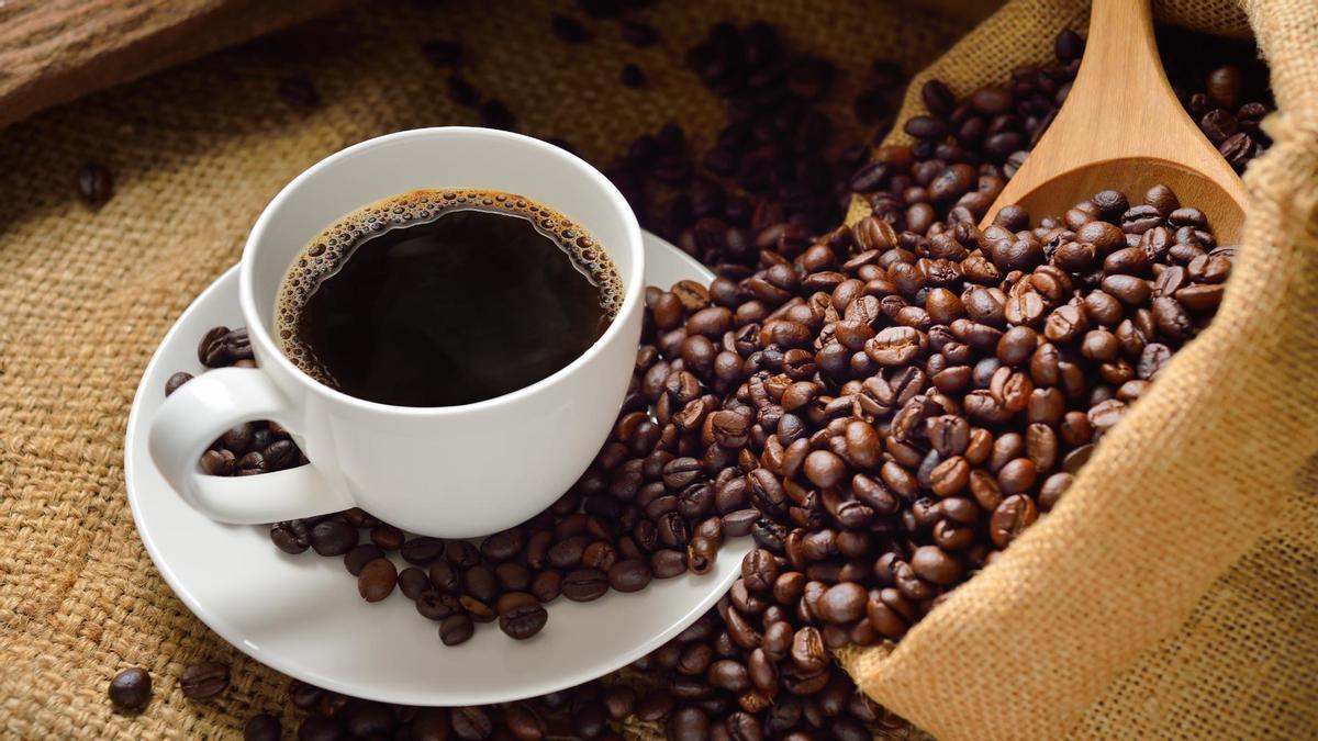 Una taza de café junto a granos de dicho producto.