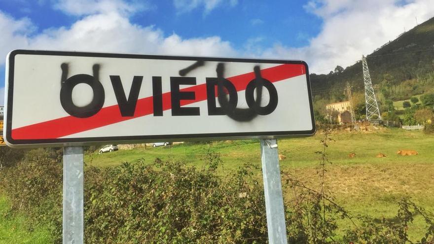 Un cartel de Oviedo con la toponimia en asturiano grafiteada por encima.
