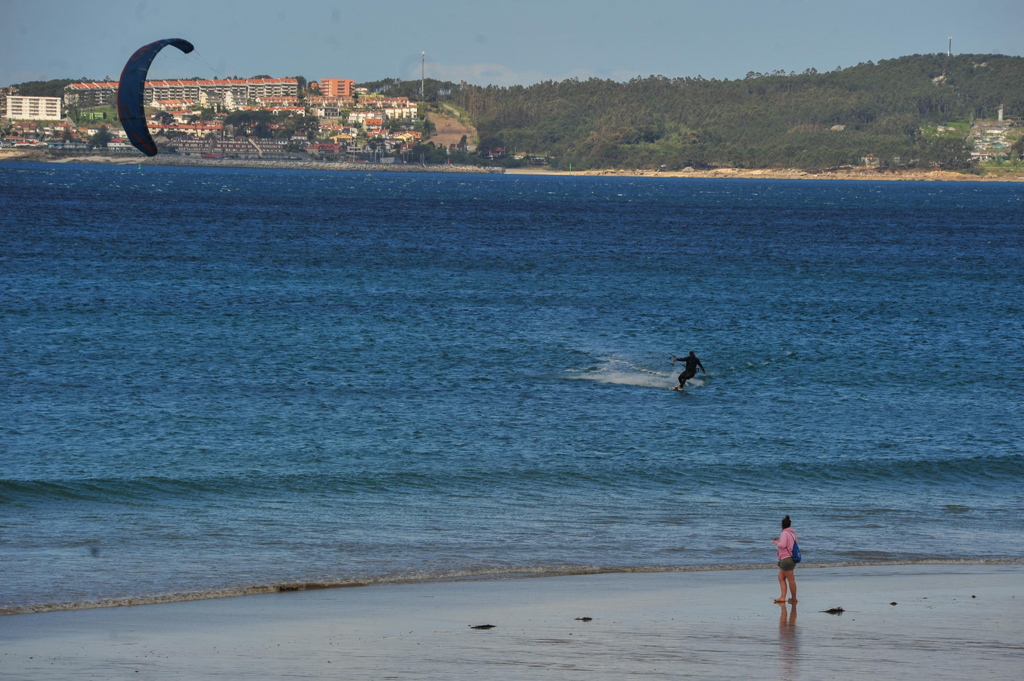 Una joven observa desde la orilla a un &quot;kitesurfista&quot;, con San Vicente do Mar, al fondo.