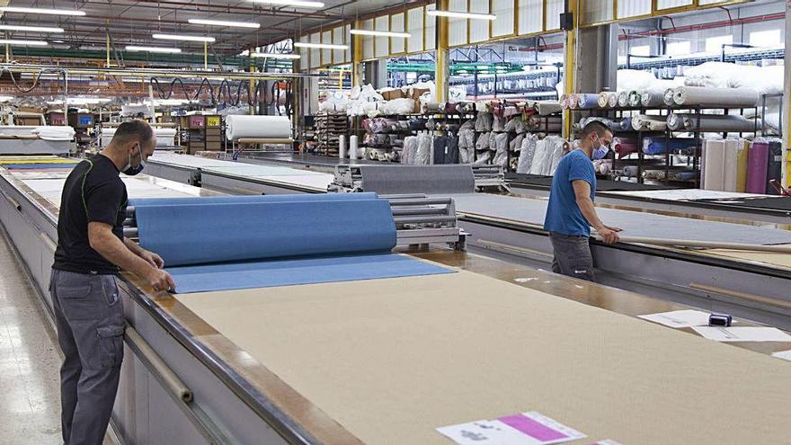 Dos empleados de la empresa Fama despliegan las telas utilizadas en las tapicerías.