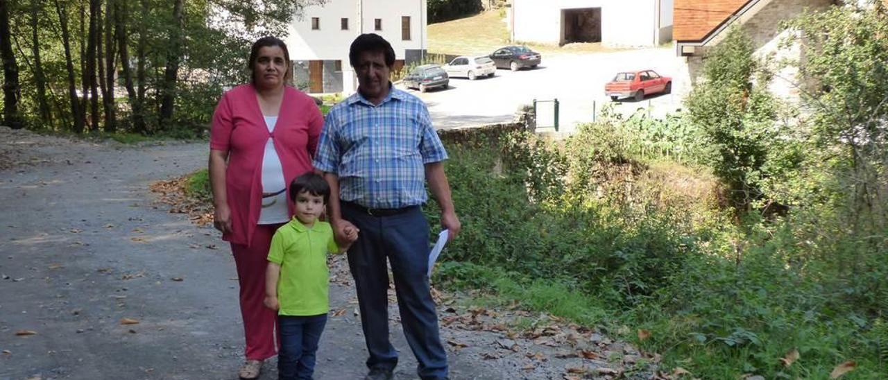 Ignacia Raquel Sánchez y Alejandro Díaz, con el pequeño Valentín Díaz, en la pista de acceso al Pumar de las Montañas, con la plaza del pueblo a sus espaldas.