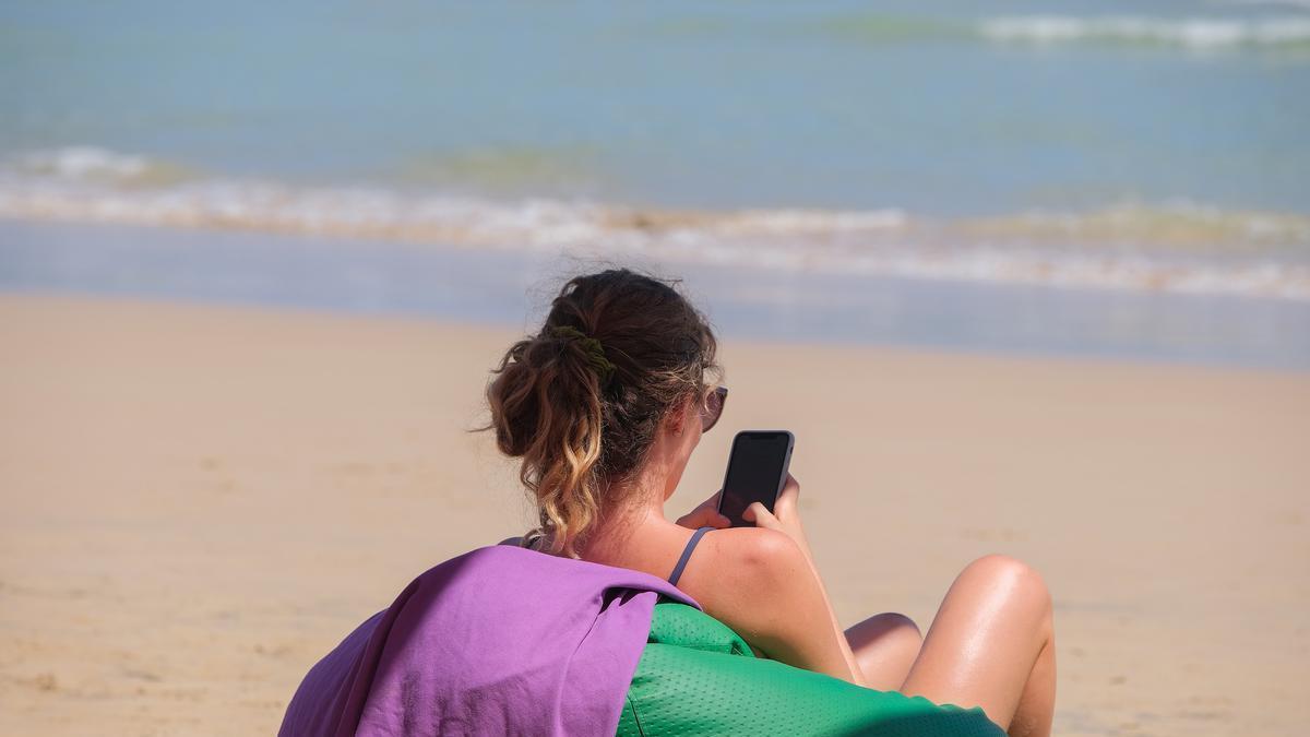 Una mujer mira el móvil sentada en la playa.