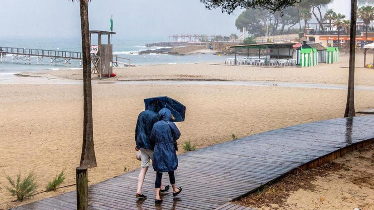 Dos personas pasean por una plahya de Mallorca bajo la lluvia.