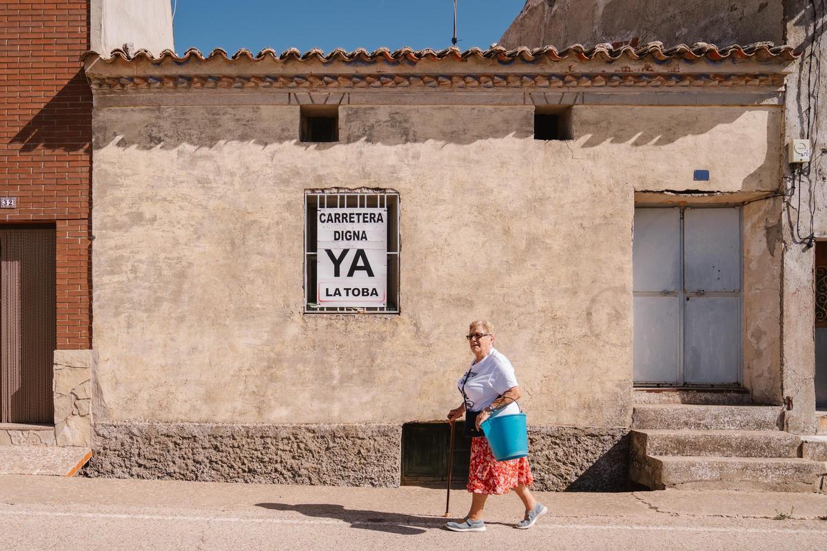Gregoria, vecina de La Toba,  pasea por el centro del pueblo, al lado de un cartel pidiendo que arreglen la casa.
