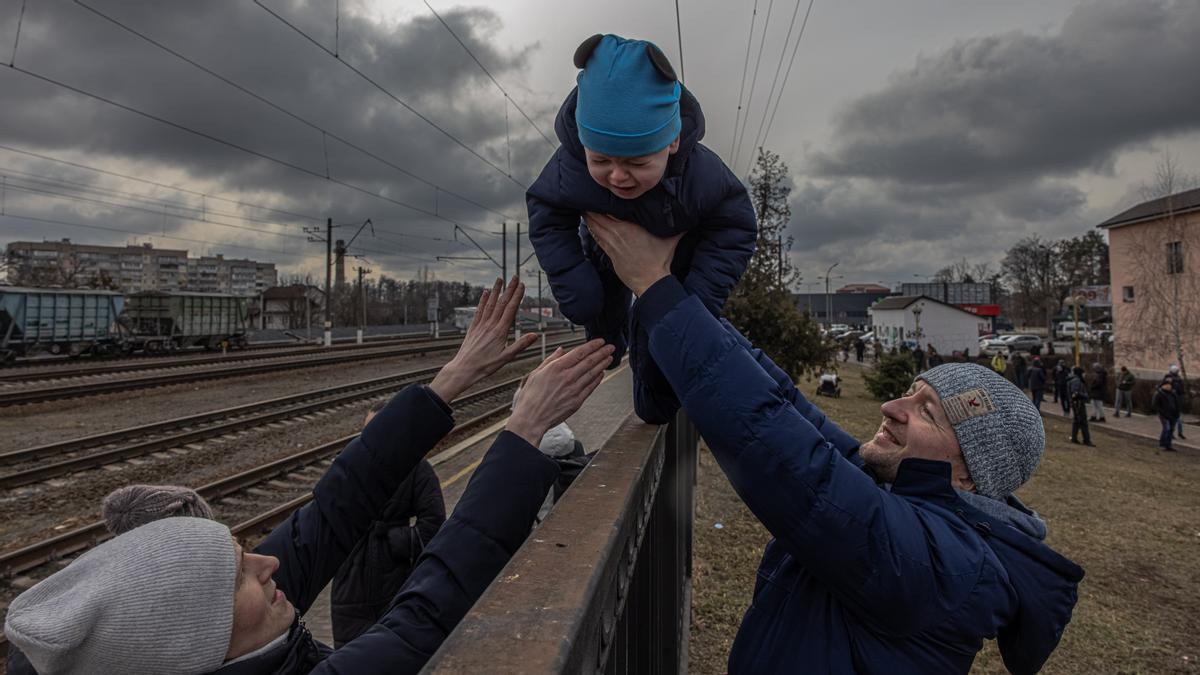 Una mujer ucraniana recoge a su hijo de los brazos de su marido a través de una valla en Irpín, antes de la evacuación de Kiev.