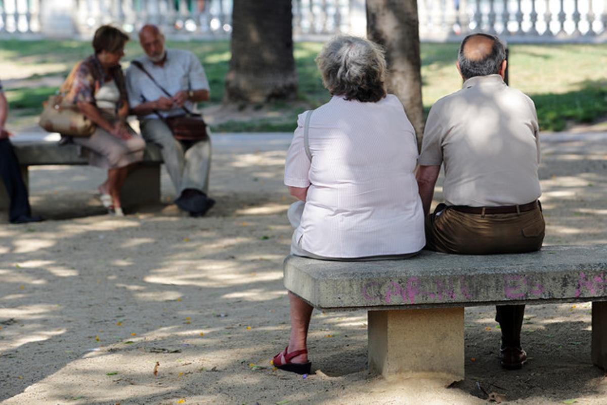 Un grup de jubilats descansen asseguts en uns bancs en un carrer de Barcelona.