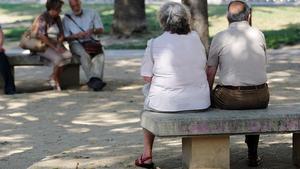 Un grup de jubilats descansen asseguts en uns bancs en un carrer de Barcelona.