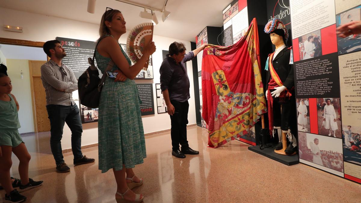 Guitarte observa la bandera tradicional del dance de Visiedo mientras la exsenadora Beatriz Martín se abanica.