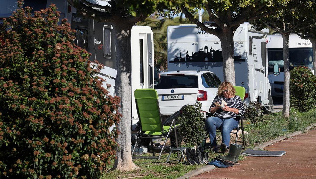 Una mujer, leyendo un libro junto a unas caravanas.