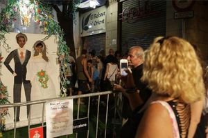 Veïns i visitants es fotografien al carrer de Puigmartí en un decorat que representa una parella de nuvis.