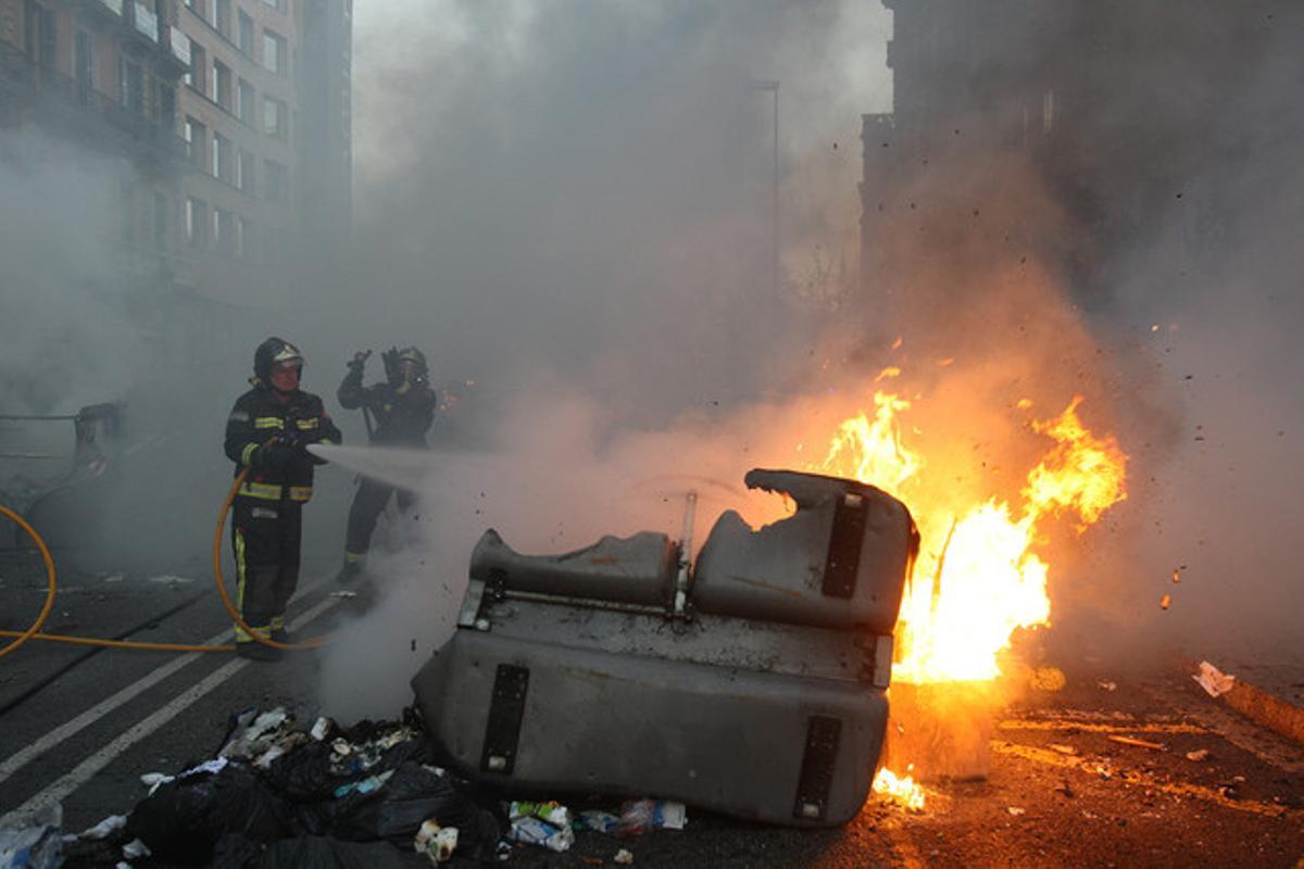 Un bombero apaga el fuego que quema un contenedor.