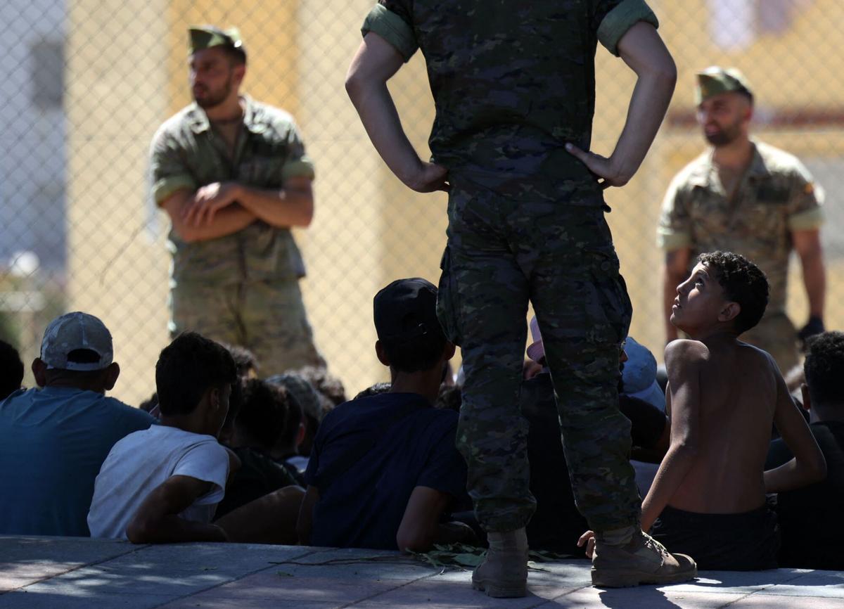 A young migrant looks at a member of the Spanish Army's 'Regulares' infantry force near the border post, prior to escorting them back to Morocco, in the Spanish enclave of Ceuta on August 2, 2026. At least 72 people died during last week's mass influx of migrants into Spain's Ceuta enclave, when tens of thousands of people mostly swam around the border post from Morocco, local officials said today. Most of the estimated 60,000 people who rushed into Spain's north African territory have returned to Morocco since the territory's largest mass migrant crossing. (Photo by Henry NICHOLLS / AFP). ALTERNATIVE CROP