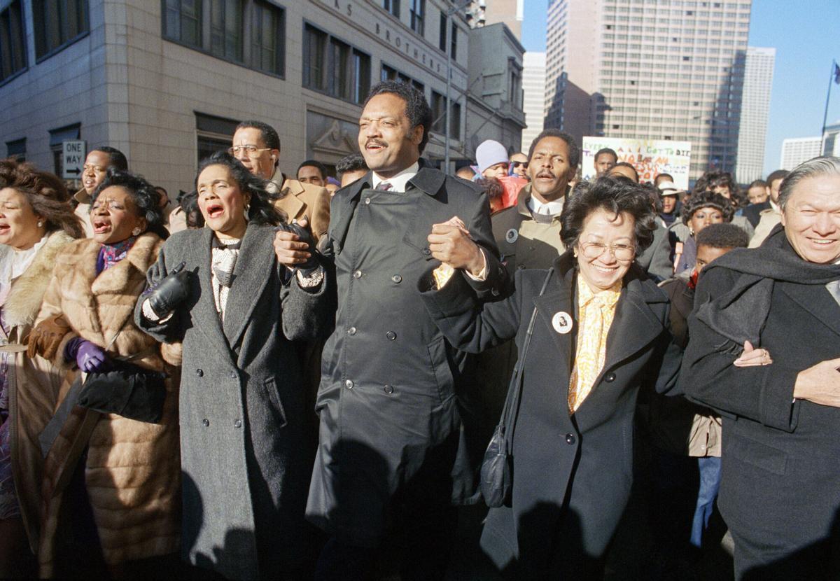 Coretta Scott King canta de la mano con el reverendo Jesse Jackson y Christine Farris, hermana del Dr. Martin Luther King, Jr., durante un desfile por la calle Peachtree de Atlanta el lunes 19 de enero de 1987 en honor al cumpleaños de King.
