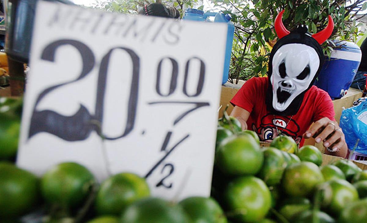 Un home llueix una màscara de Halloween mentre despatxa fruites a la seva parada del cementiri de Manila.