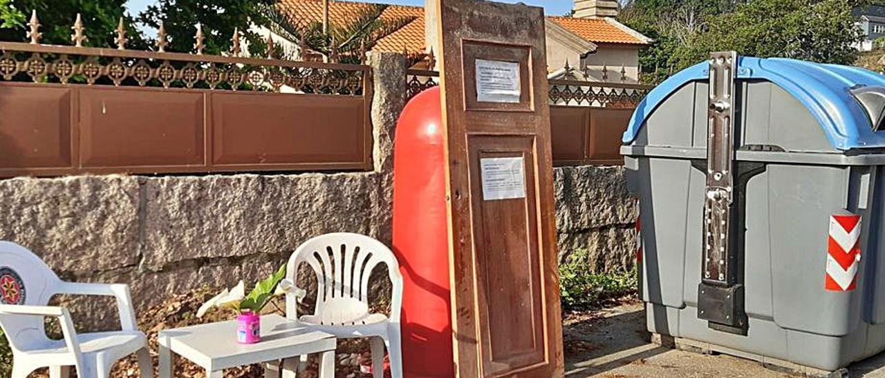 Así amaneció estos días el cruce hacia Espiñeira, en Aldán. Todo un salón-recibidor con vistas exteriores. Mesa, sillas, flores y una puerta. Pero no se confundan. No se trata de ningún intento de apropiarse del espacio público, sino de un toque de atención en toda regla. Parece que es habitual usar este espacio como un improvisado punto limpio, dejando todo tipo de enseres y voluminosos. Por eso en la puerta hay un cartel informativo explicando para que sirve cada contenedor y con el teléfono del punto limpio. ¡Es difícil no pillar una indirecta tan directa!