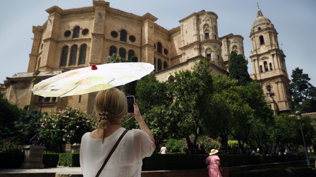 Una turista fotografía la Catedral de Málaga con el patio de los naranjos en primer témino.