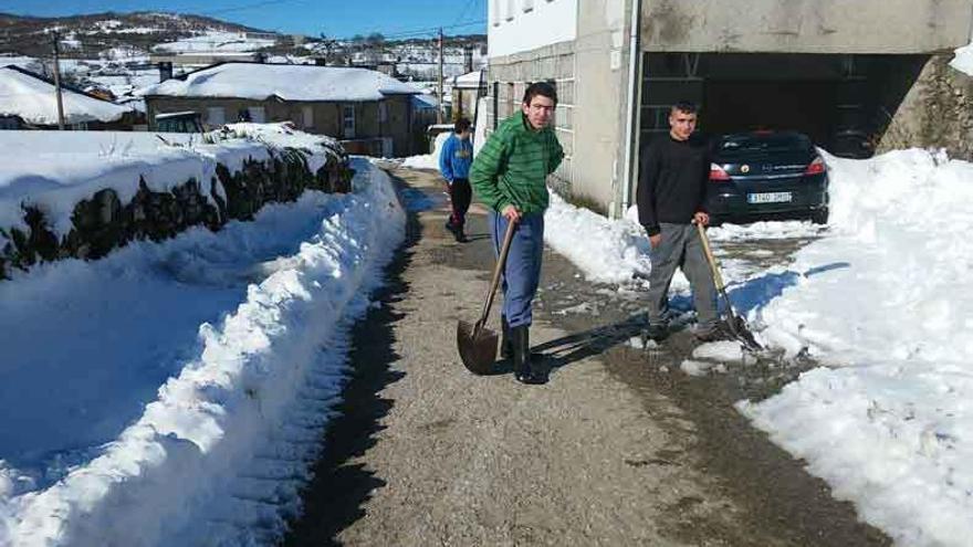 Jóvenes de Villanueva de la Sierra limpian de nieve una calle nevada en febrero.