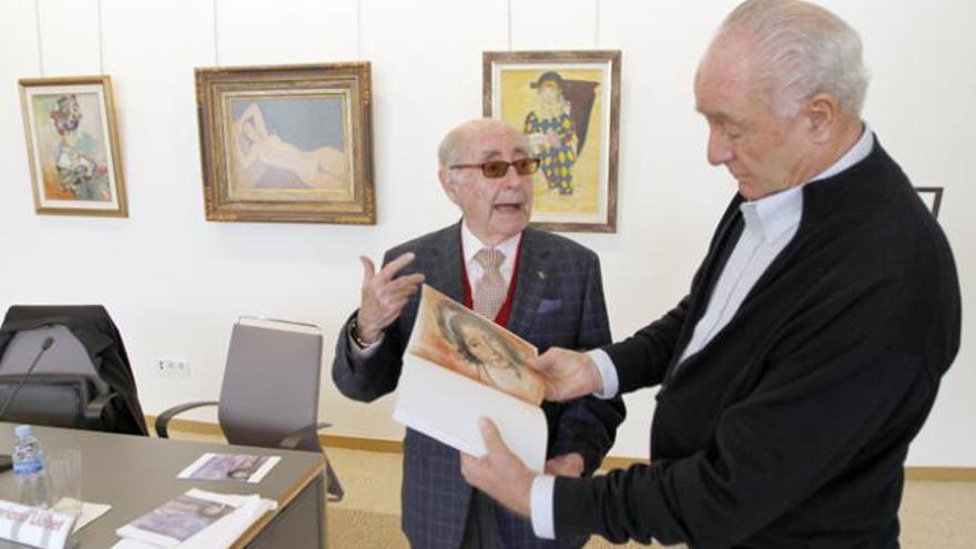 Roselló, con el catálogo de la muestra del Círculo de Bellas Artes de Madrid, mostrando uno de los cuadros de Llobet, a su lado.